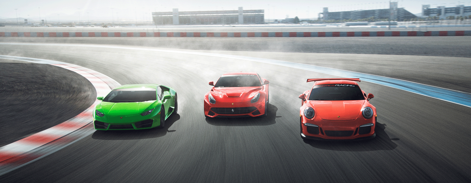 Three sports cars, a green, a red, and an orange one, speed around a racetrack curve. Dust trails follow, conveying motion and excitement.
