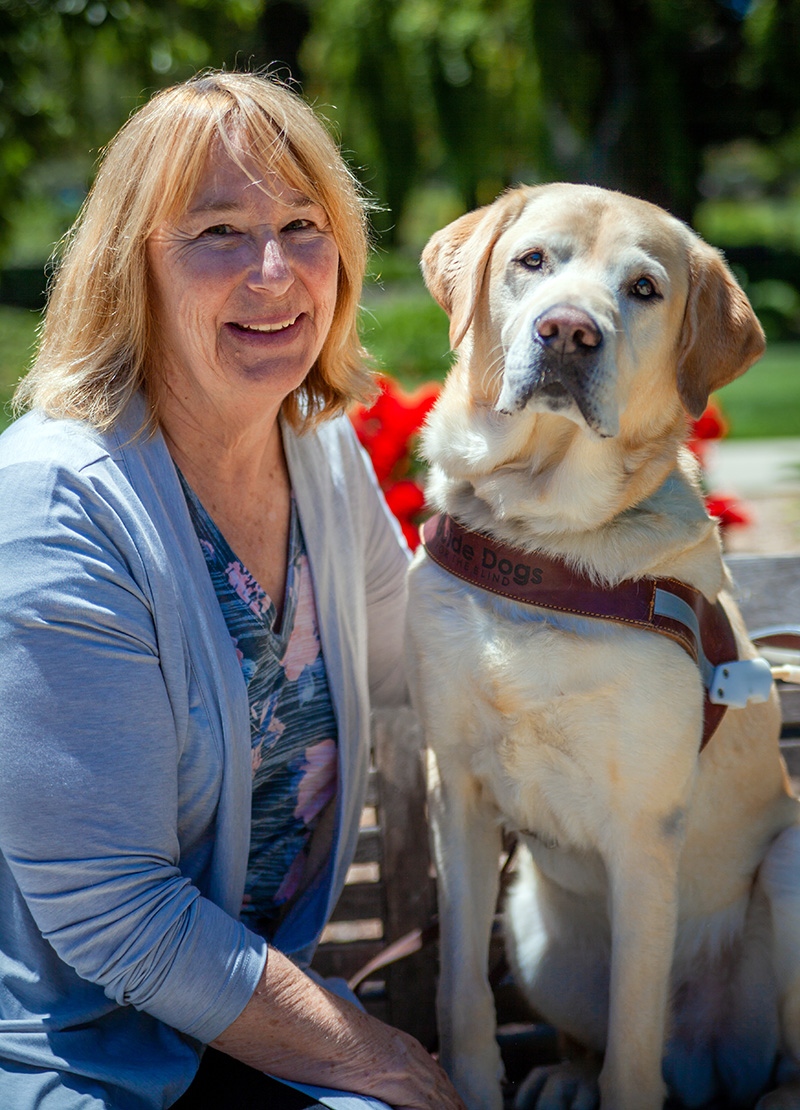 Claudia Barkmeier seated next to a yellow Lab guide dog.
