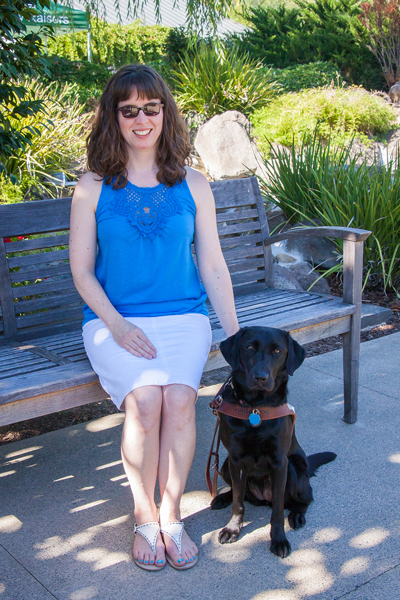 Leanne sits on a bench with her black Lab guide dog Eva.