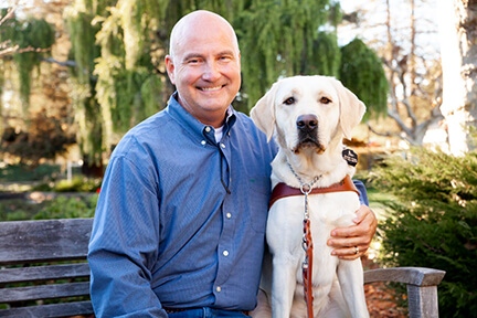 A portrait of Scott Wilcock sitting next to his yellow Lab guide dog, Sailor.