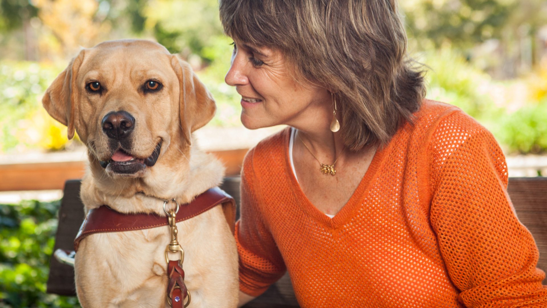 A female GDB graduate smiles while looking at her yellow Lab guide dog