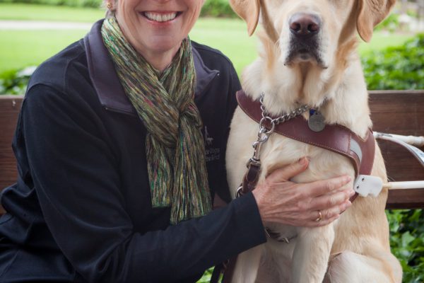 GDB employee Joan Scott sittingon a bench next to a yellow Lab guide dog.