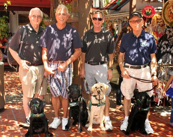 Puppy raisers pose on the sidewalk with their guide dogs puppies (one yellow and three black Lab).
