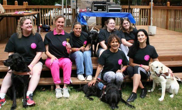 Seven members of Mommies with Guides pose with their black and pink t-shirts and guide dogs