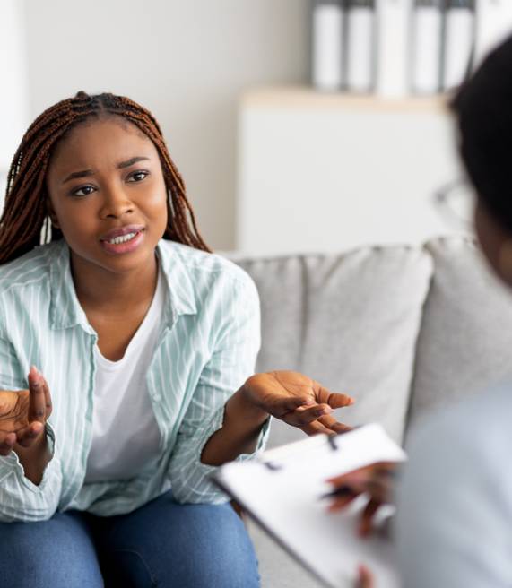 young worried black woman having counseling session with psychotherapist at clinic