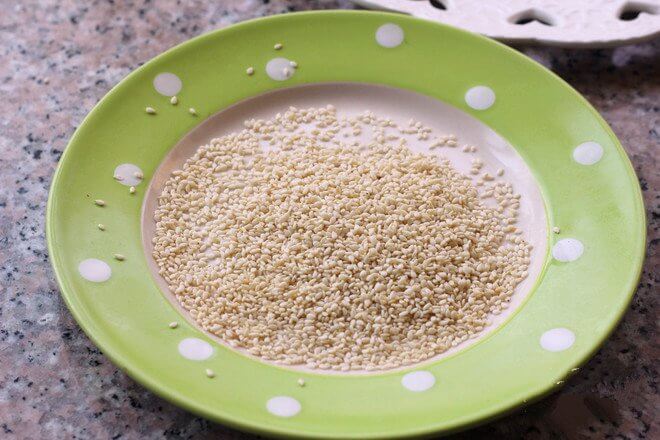 White sesame seeds are poured onto a plate.