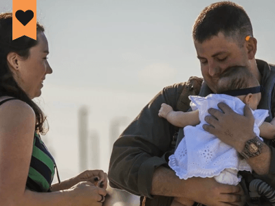 us military man holding his baby with is wife standing to the left of him and the child facing them