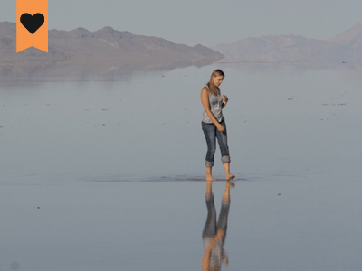 woman walking on a lake shore with her reflection showing in the water and desert hills in the background
