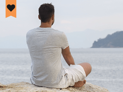 man stting indian style on a rock overlooking the ocean