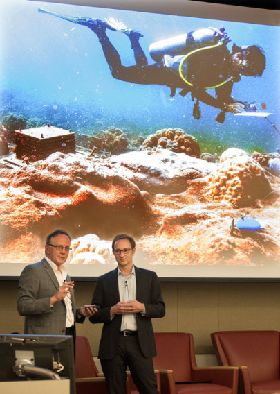Steve Ringman and Craig Welch standing infront of a screen that is showing a photo of a man scuba diving.
