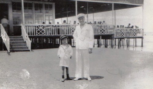 Victor Vidal and his son Nisso; both wearing the white sharkskin suit. In the background: Casino Fouad in Rass-el-Barr, where many high middle-class Jews enjoyed a whole summer of leisure. After a morning swim on the Mediterranean, and a well earned 'siesta', they used to welcome the evenings with a slow and relaxing walk along the Nile, offering to the ladies those famous jasmine-necklaces, spreading all over their exquisite and unforgettable Jasmine scent