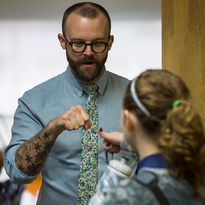 Teacher gives fist-bump to student standing outside doorway