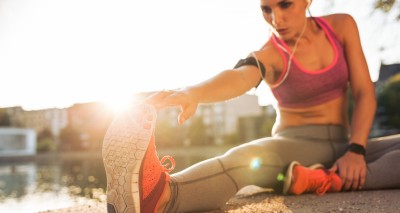 Young woman runner stretching legs before doing her summer workout. Sportswoman warming up before outdoor workout.