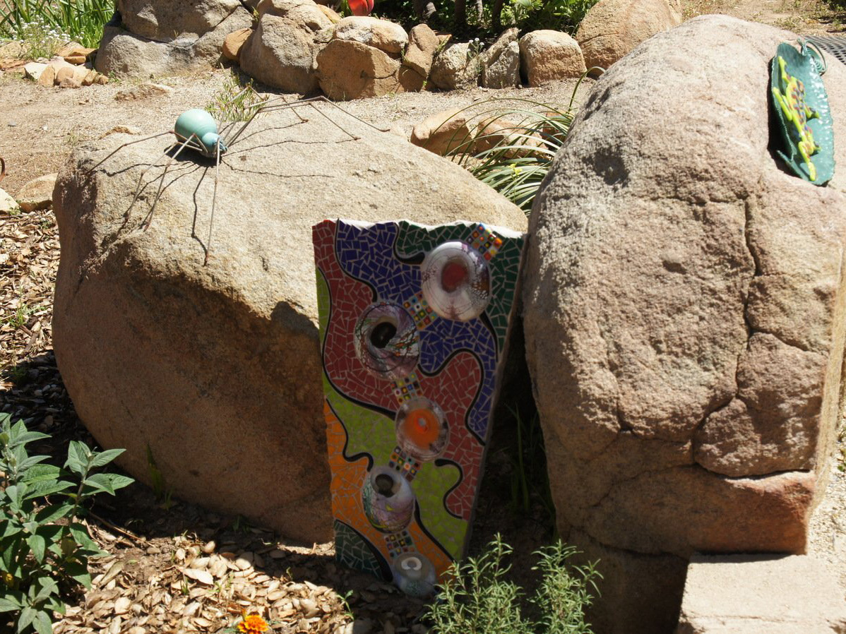 Small mosaic rock garden art piece next to boulder